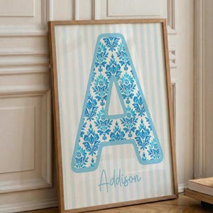 Puede incluir: Arte mural enmarcado con una gran letra "A" azul con un patrón floral. La letra se encuentra sobre un fondo a rayas azules y blancas. El nombre "Addison" está escrito en cursiva debajo.
