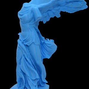 Puede incluir: Estatua azul claro de la Victoria de Samotracia, una escultura helenística. La figura sin cabeza se representa con drapeado fluido y alas extendidas, montada sobre una base rectangular. La estatua está sobre un fondo negro.