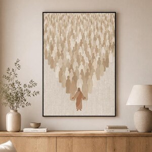 Könnte beinhalten: Ein gerahmter Kunstdruck zeigt eine Menge von Figuren in verschiedenen Beigetönen, die sich auf eine zentrale Figur in einem rotbraunen Gewand zubewegen. Das Kunstwerk ist vor einem neutralen Hintergrund platziert und erzeugt eine ruhige Atmosphäre. Der Druck befindet sich über einem Holzschrank.