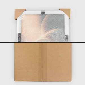 K&ouml;nnte beinhalten: Ein gerahmtes Kunstwerk, verpackt in Luftpolsterfolie und gesch&uuml;tzt durch Ecksch&uuml;tzer aus Pappe, befindet sich in einem braunen Karton. Das Kunstwerk zeigt ein weiches, abstraktes Design mit warmen, leuchtenden Farben.