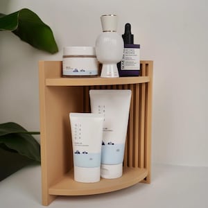 May include: A light tan corner shelf holds five skincare products: a round jar, a white bottle with a gold rim, a dark purple dropper bottle labelled Retinol Intense, and two white tubes labelled 1025 Dokdo, all featuring blue and white accents.