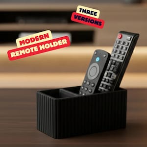 Könnte beinhalten: Ein moderner, schwarzer Fernbedienungshalter mit zwei Fächern, der zwei schwarze Fernbedienungen hält. Der Halter hat ein geriffeltes Design. Der Text auf dem Bild lautet "MODERN REMOTE HOLDER" und "THREE VERSIONS".