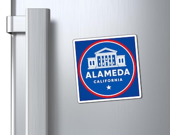 May include: A square magnet with a blue background and a red circular border. The magnet features a white illustration of a building and the text "ALAMEDA CALIFORNIA" in white. A white star is at the bottom.