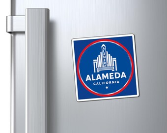 May include: A square magnet with a blue background and a red circular border. The magnet features the text "ALAMEDA CALIFORNIA" in white, along with a stylized architectural design. A small white star is at the bottom.