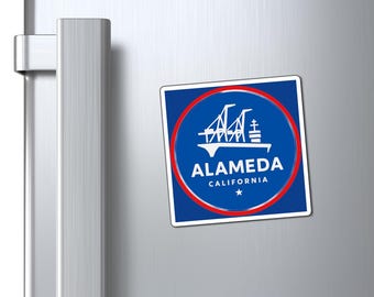 May include: A square magnet featuring a blue background with a red circular border. The magnet displays the word "ALAMEDA" in white, along with a bridge illustration and the text "CALIFORNIA".