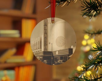 May include: Round Christmas ornament featuring a sepia-toned image of the Alameda Theatre. The word "ALAMEDA" is vertically displayed on the left side of the building. The ornament hangs from a red ribbon.