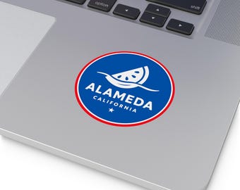May include: A round sticker featuring the text "ALAMEDA CALIFORNIA" in white, with a blue background and a red border. The design includes a white watermelon slice and a star.
