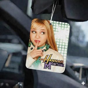 May include: Rectangular air freshener featuring a portrait of Hannah Montana with a finger to her lips. The air freshener has the Hannah Montana logo in the lower right corner and is hanging from a white string.