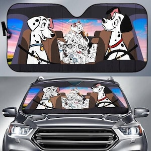 May include: Black car sunshade featuring a Dalmatian family cartoon design. The sunshade depicts two adult Dalmatians in the front seats and a group of puppies in the back. The background shows a sunset scene.