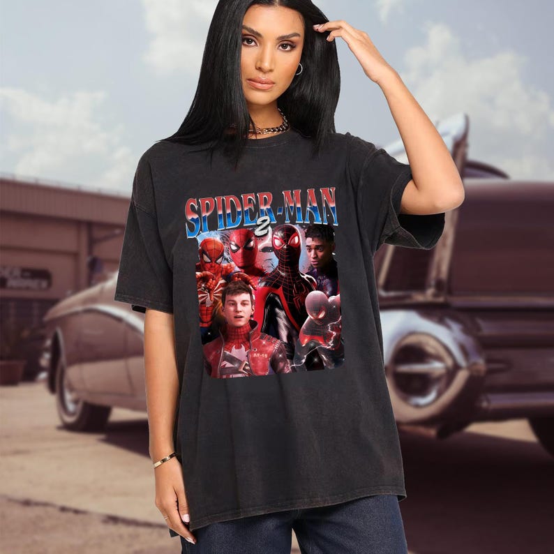 May include: Black t-shirt with a Spider-Man 2 graphic. The design showcases multiple Spider-Man characters in red, black, and blue. The text "SPIDER-MAN 2" is displayed across the top in a retro style.