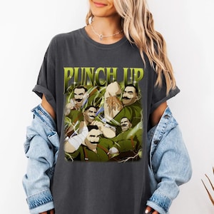 May include: Dark gray t-shirt featuring a graphic with the text "PUNCH UP" in yellow and green. The graphic depicts several cartoon figures with mustaches and green outfits. The figures are in various action poses.