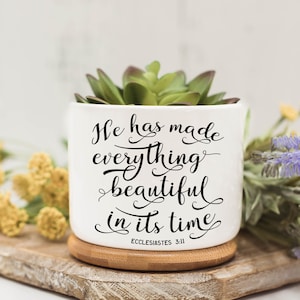 May include: White ceramic planter with a succulent plant inside. The planter has a black inscription that reads "He has made everything beautiful in its time" with the scripture reference "Ecclesiastes 3:11" below the text.