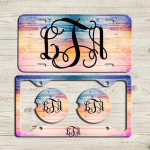 May include: A set of two car accessories featuring a colorful woodgrain design with a monogram. The set includes a license plate frame and two matching coasters.