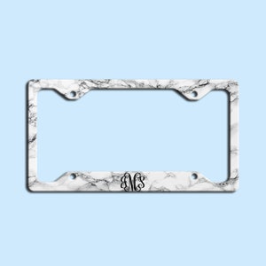 May include: White marble license plate frame with a black monogram "EMS" in the center.