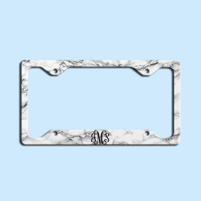 May include: White marble license plate frame with a black monogram "EMS" in the center.