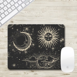May include: A black mouse pad with a celestial design featuring a crescent moon, sun, and stars. The moon and sun have faces drawn on them.