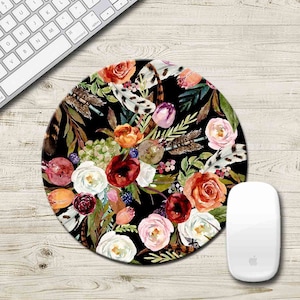 May include: Round mouse pad with a floral design. The design features red, pink, white, and orange flowers with green leaves and feathers on a black background.