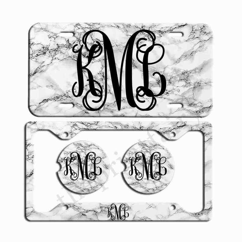 May include: White marble license plate frame with two matching beverage coasters. All three items feature a black monogram "KMC" in a decorative script font.