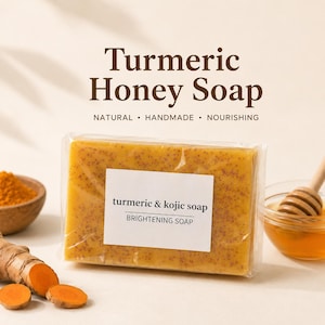 May include: A rectangular bar of turmeric and honey soap wrapped in clear plastic. The label reads "Turmeric Honey Soap NATURAL • HANDMADE • NOURISHING" and "turmeric & kojic soap BRIGHTENING SOAP". Turmeric powder and honey are visible nearby.