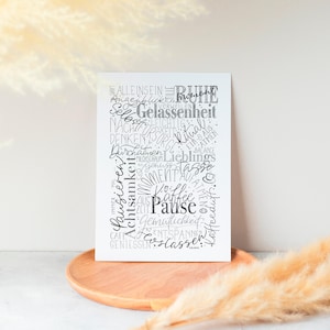 Könnte beinhalten: Ein weißer, rechteckiger Kunstdruck mit schwarzer Schrift auf einem Holztablett. Der Druck zeigt Wörter wie "Pause" und "Entspannen" in einem Wordcloud-Design. Der Hintergrund ist neutralfarben mit getrocknetem Ziergras.
