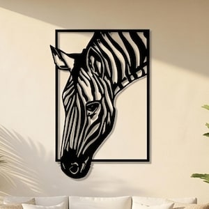 May include: Black metal wall art featuring a zebra's head and neck, framed in a rectangular shape. The zebra's stripes are clearly defined, creating a striking contrast against the wall. The artwork is mounted on a light-colored wall, with a sofa and plants in the foreground.