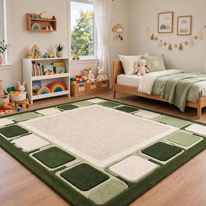 May include: A rectangular area rug featuring a large, solid beige center panel surrounded by a border of alternating dark green, light green, and cream-colored square blocks, creating a geometric frame pattern on a soft-textured surface.
