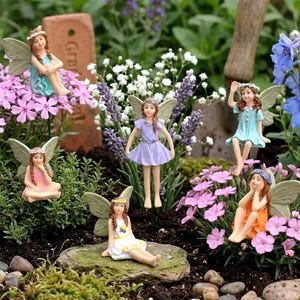 以下が含まれることがあります： 繊細な羽と花の冠を持つ妖精の庭の置物のコレクション。妖精たちは、青、ピンク、オレンジ、紫など、さまざまなパステルカラーの衣装を着ています。鮮やかなピンクと紫の花の中に配置され、気まぐれな庭のシーンを作り出しています。