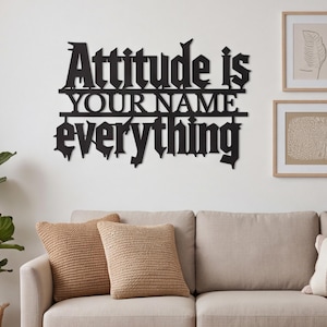 May include: A black metal wall sign featuring the text Attitude is YOUR NAME everything in a stylized gothic font. The letters are connected by horizontal lines, creating a single piece of wall decor with a bold, dark, and sharp appearance.