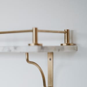 Peut inclure: Étagère murale avec un dessus en marbre et des supports en laiton. Le design est minimaliste, avec des lignes épurées et une palette de couleurs neutres. Les supports en laiton sont incurvés, ajoutant une touche d'élégance. Idéale pour exposer des objets décoratifs.