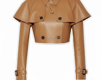 May include: A tan leather cropped trench coat with a double-breasted front, a notched collar, and a cape-like overlay. The coat features long sleeves with buckle details at the cuffs and black buttons. The overall design is a modern take on a classic style.
