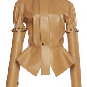 May include: A tan-colored leather jacket with a high collar and a peplum waist. The jacket features long sleeves with buttoned cuffs and a button closure down the front. The design is sleek and modern, suitable for various occasions.