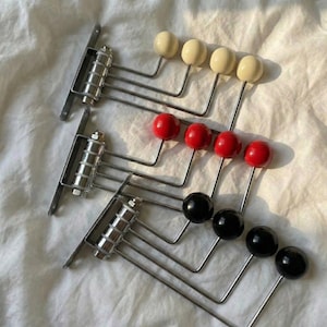 May include: Three vintage coat racks with metal brackets and rods. Each rack has four round knobs in cream, red, and black. The racks are arranged on a white, textured surface.