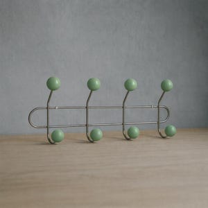 May include: A contemporary coat rack for wall mounting, featuring a silver metal frame and eight light green ball hooks. The hooks are arranged in pairs, with four at the top and four at the bottom. Ideal for hanging coats, hats, or other items.
