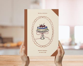May include: A recipe journal with a cream-colored cover and a brown spine. The cover features a cake illustration inside a decorative oval frame. The text "MICHELLE SAMUELS" is at the top, and "RECIPE JOURNAL" and "from fridge to plate" are at the bottom.