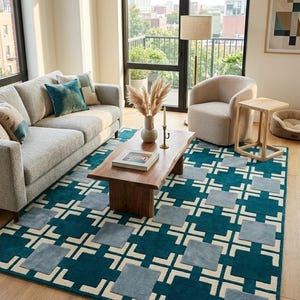 May include: A rectangular area rug featuring a deep teal background with a repeating geometric pattern of light blue squares and white intersecting lines. The rug is positioned on a light wood floor beneath a wooden coffee table in a living room.