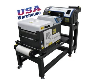 May include: A large industrial printing machine with a white and dark gray chassis, featuring a roll of film at the front, a digital control panel, and a prominent blue and red logo that reads USA Warehouse. The unit is mounted on a black metal stand.