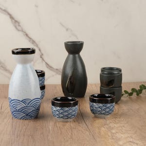 以下が含まれることがあります： 日本の酒器セット。 白い波模様のボトル1本、黒いボトル1本、小さなカップがいくつかあります。 カップと白いボトルには青い波模様があります。