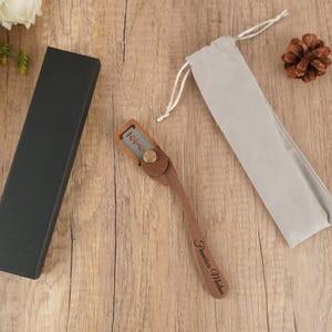 Op de afbeelding: Een houten scheermes met een zilveren mes en een messing sluiting, gepresenteerd met een zwarte doos en een grijze trekkoordzak. De scheermeshandgreep is gegraveerd met de naam "Francisco Medina".