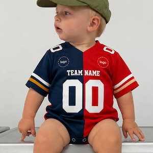 May include: A toddler wears an olive green baseball cap and a split-color jersey-style bodysuit. The bodysuit features a navy blue right side and a red left side, with white text reading TEAM NAME and the number 00 centered on the front chest.