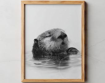 May include: Black and white framed print featuring a sea otter floating in water. The otter's face is visible, with its eyes closed. The frame is made of light-colored wood. The text "PIXEL TO PRINT" is at the top.