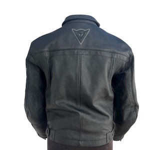 May include: Black leather motorcycle jacket with a collar and a logo on the upper back. The jacket has a classic design with ribbed detailing on the shoulders and a belt at the waist.
