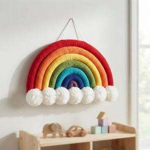 Può includere: Una decorazione da parete a forma di arcobaleno lavorata a maglia con archi concentrici in rosso, arancione, giallo, verde, blu e viola. Il bordo inferiore è decorato con una fila di sette pon-pon bianchi soffici e un filo per appenderlo.