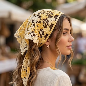Könnte beinhalten: Ein gelb-cremefarbener Häkelschal mit floralem Muster. Die Kopfbedeckung ist hinten gebunden und fällt über den Hinterkopf. Der Schal ist aus einem weichen, leichten Material gefertigt.