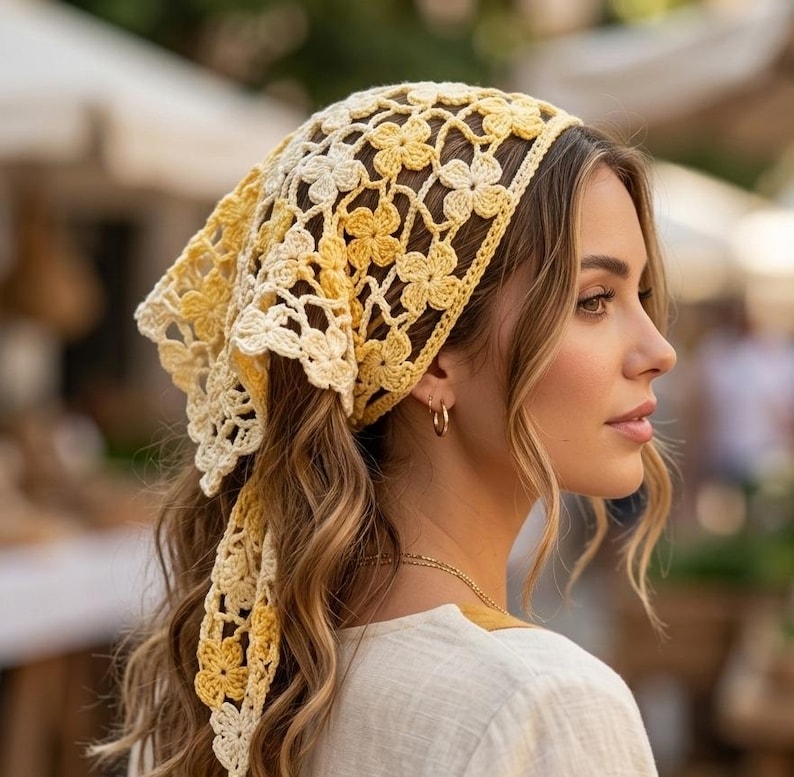 May include: A yellow and cream-colored crochet headscarf with a floral pattern. The head covering is tied at the back and drapes down the back of the head. The headscarf is made of a soft, lightweight material.