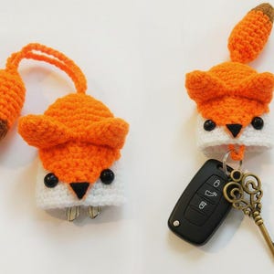 May include: Two handmade crochet fox keychains. The foxes are orange and white with black eyes and a black nose. One keychain has a key attached, and the other has keys inside. The fox tails are orange with a brown tip.