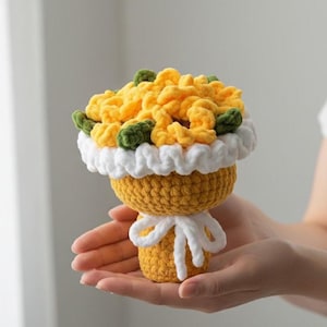 Puede incluir: Un ramo de crochet hecho a mano con flores amarillas y hojas verdes, un ribete blanco con volantes y una base amarilla atada con un lazo blanco. Un artículo único y artesanal.