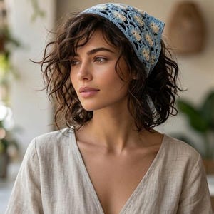 May include: A light blue and cream-colored crochet headscarf with a floral pattern. The headscarf is tied at the back. The person is wearing a beige v-neck top.