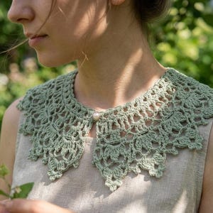 Puede incluir: Un cuello de ganchillo verde salvia con un dise&ntilde;o calado delicado. El cuello se abrocha con un solo bot&oacute;n de perla. El cuello se lleva sobre una camiseta de color neutro, creando un look de inspiraci&oacute;n vintage.