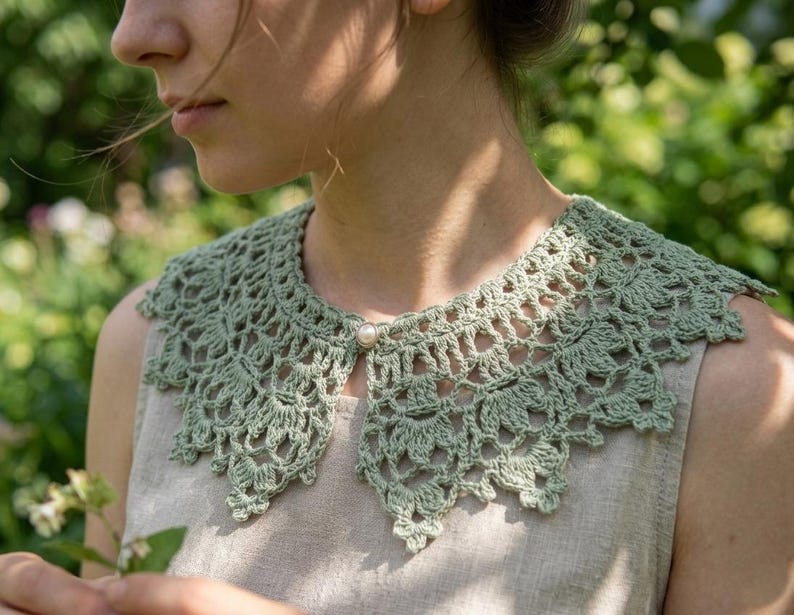 Puede incluir: Un cuello de ganchillo verde salvia con un dise&ntilde;o calado delicado. El cuello se abrocha con un solo bot&oacute;n de perla. El cuello se lleva sobre una camiseta de color neutro, creando un look de inspiraci&oacute;n vintage.