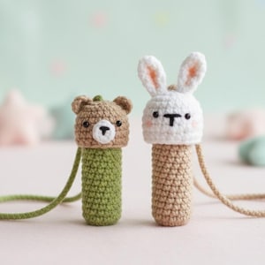 May include: Two handmade crochet animal pendants: a bear with a brown head and green body, and a bunny with a white head and tan body. Both have black eyes and a small black nose. Each pendant has a matching cord for wearing.